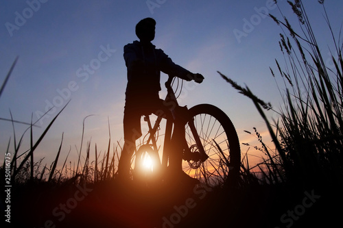 Silhouette of a cyclist against the sunset sky with sun and sunlight, copy space 