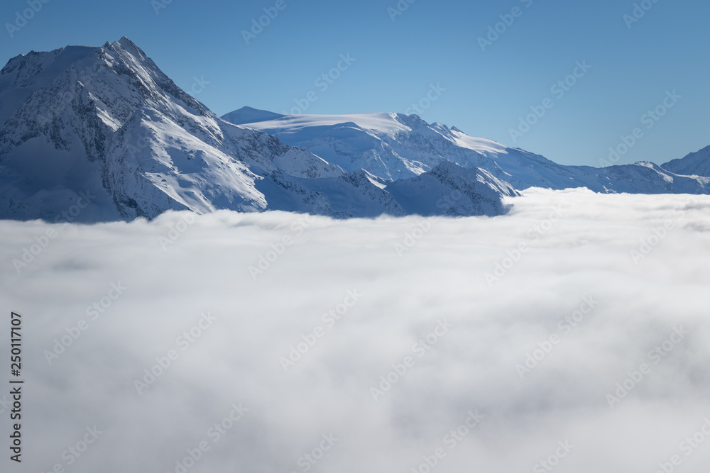 Fototapeta premium Mountain peaks covered in snow above clouds in La Plagne, French Savoy Alps. Winter scenic scenery, blue sky and stunning views.