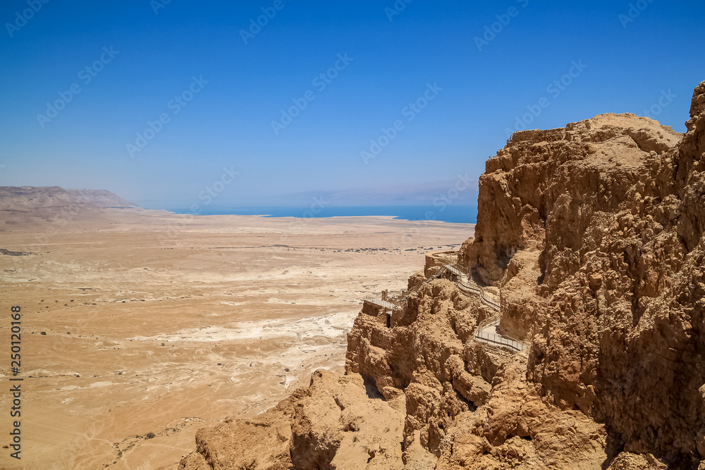View of a pedestrian walkway up the side of Masada mountain, with Dead Sea in hazy background
