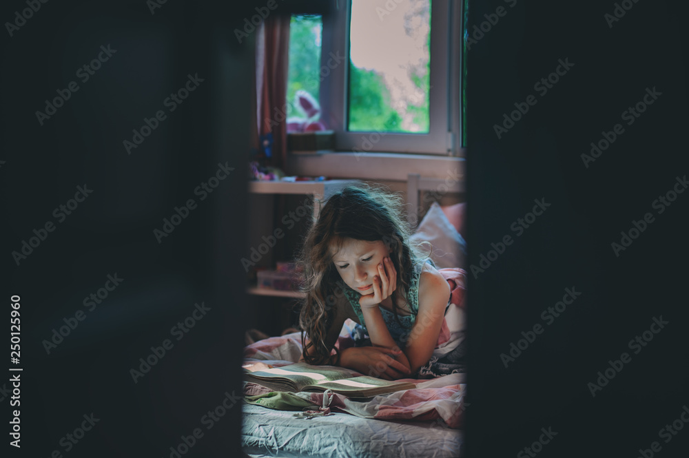 thoughtful kid girl reading book alone in her room in the veening or early morning