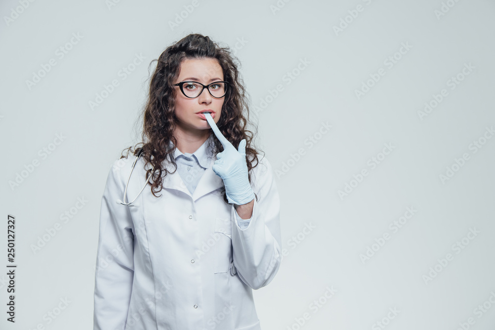 Beautiful nurse with black hair. Wearing blue medical uniformed handbags. In black glasses and gloves on a gray background and looking at the camera, a portrait. Beautiful nurse with black hair. Wearing blue medical uniformed handbags. In black glasses and gloves on a gray background and looking at the camera, a portrait.