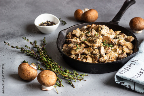 Meat stewed with mushroom and thyme in a cast-iron pan. Grey concrete background. Copy space. 