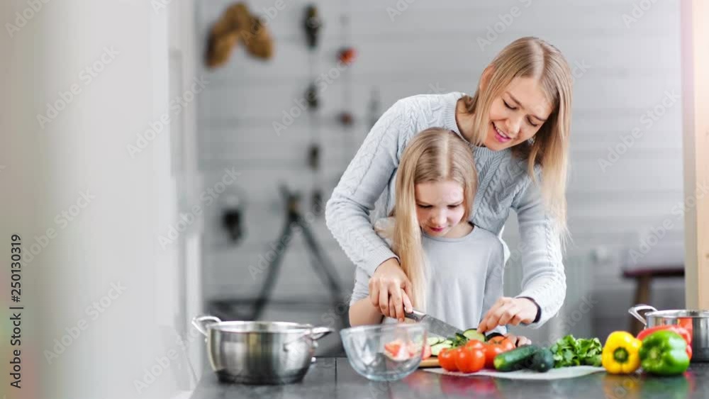 Smiling mother and girl preparing salad in a bowl in a kitchen Smiling mother and girl preparing salad in a bowl in a kitchen