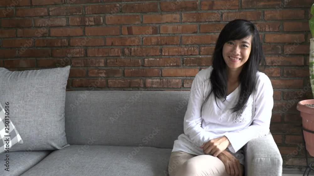 smiling happy asian woman sitting on a couch in her room smiling happy asian woman sitting on a couch in her room