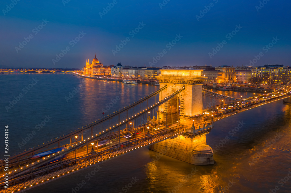 Fototapeta premium Budapest, Hungary - Aerial view of the famous illuminated Szechenyi Chain Bridge at blue hour with Parliament building at the background and clear blue sky