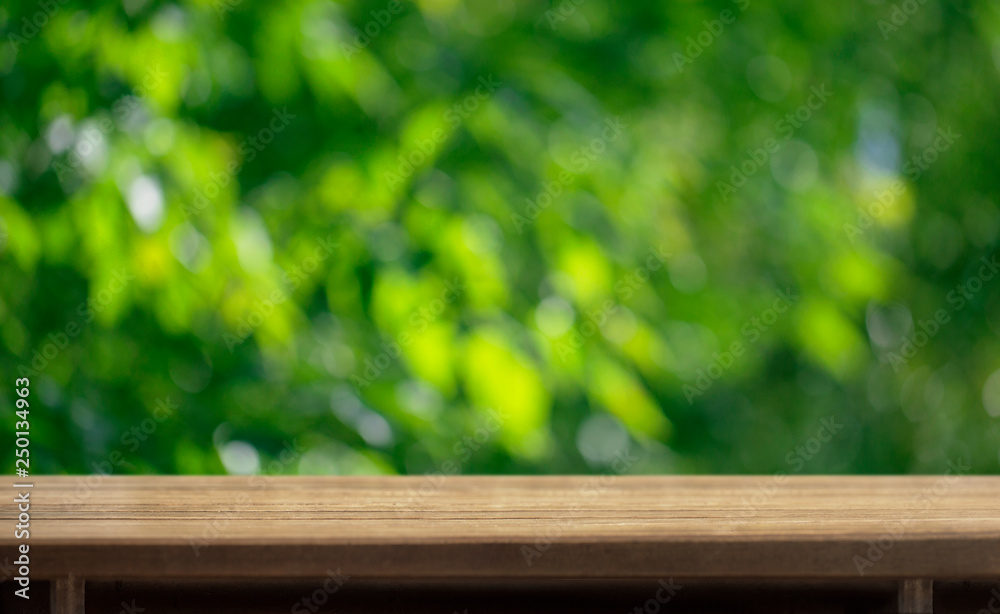 Wooden table surface and blurred leaves of a tree in the background Wooden table surface and blurred leaves of a tree in the background