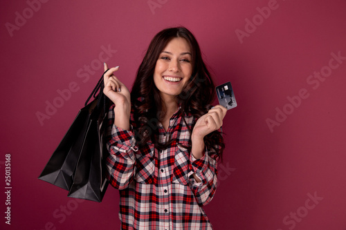 Smiling young woman with bags and credit card posing in a studio isolated.