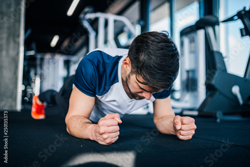 Young athletic man in sport clothing planking while exercising in the gym.