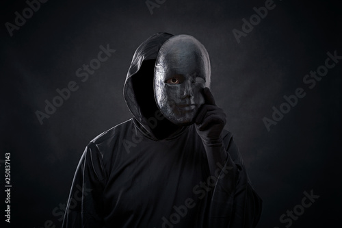 Scary figure in hooded cloak with mask in hand 