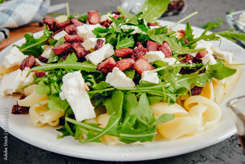 Dish with Arugula on a white plate. Green, fresh arugula on a plate, with white cheese and pasta on a stone countertop. The concept of preparing a fresh and healthy salad. Caring for health.