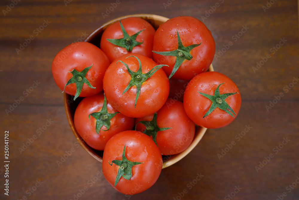 Red tomatoes are in a clay brown bowl on a brown wooden table Red tomatoes are in a clay brown bowl on a brown wooden table