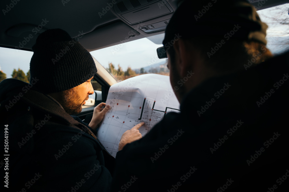 Two robbers planning and pointing on the blueprint(map) their objective while holding their guns.