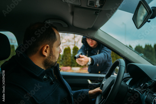 Armed bandit hijacking a middle-aged man's car. © qunica.com