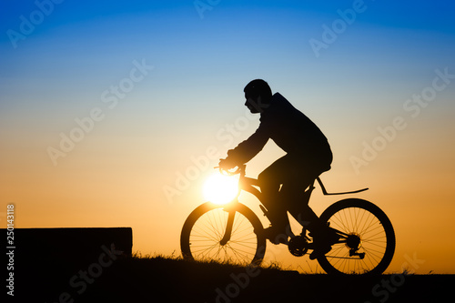 Silhouette of a young man riding a bicycle at sunset