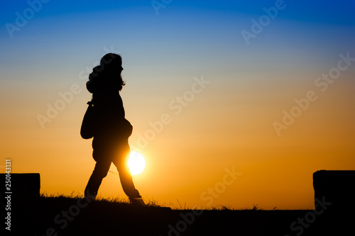 Silhouette of a young woman enjoying walking on the sunset