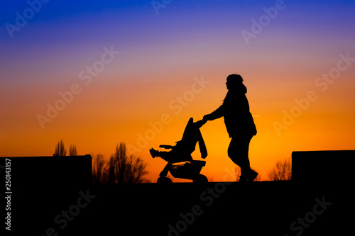 Silhouette of a young mother pushing a baby in a carriage at sunset