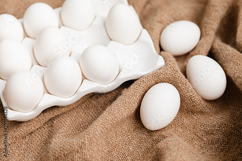 White Chicken Eggs In Ceramic Carton Holder On Burlap Background