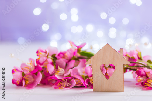 Closeup wooden house with hole in form of heart with tender pink cherry flowers on blurred lilac background with bokeh.