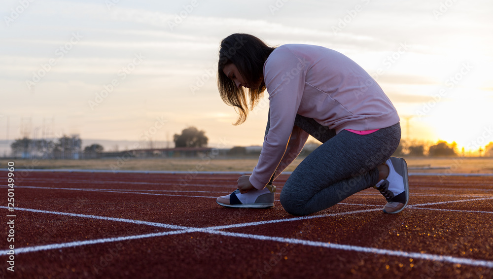 Pretty young girl doing sports on running tracks with pink cap and sweatshirt