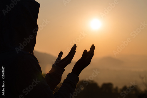 Silhouette of young  human hands open palm up worship and praying to god  at sunrise, Christian Religion concept background.