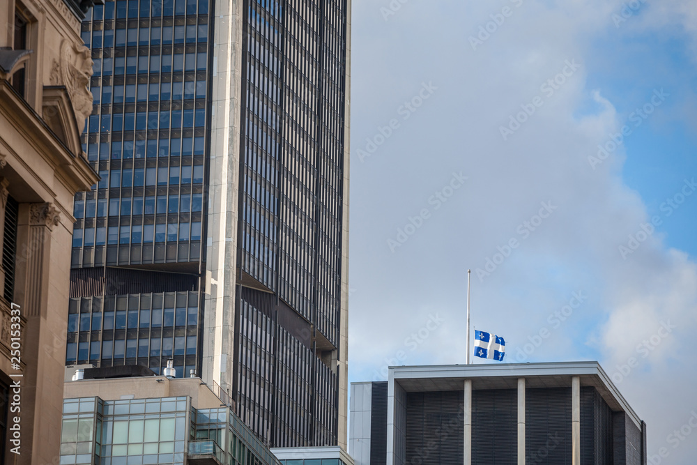 Flag of Quebec waiving in Old Montreal, Quebec, Canada, surrounded by modern office buildings and old skyscrapers. Also known as Fleur de Lys, or fleurdelise, it's the symbol of the province of Quebec