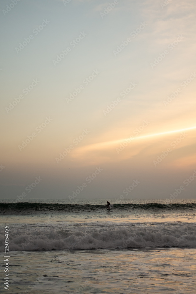 A stand up surfer is riding a wave alone during sunset in Bali, Indonesia
