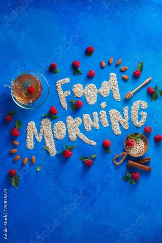 Good Morning concept with words written with oatmeal, raspberries and cinnamon. Healthy eating flat lay on a blue background with copy space.