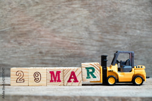 Toy forklift hold block R to complete word 29mar on wood background (Concept for calendar date 29 in month March) photo