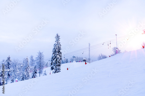 Snow-covered ski slope in the mountains with a lift and skiers skating away