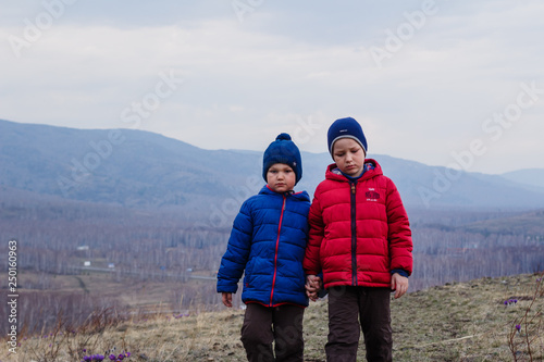 tired children walk outdoors in the mountains . Two boys in warm jackets and hats