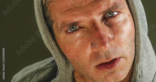 close up sweaty face portrait of young attractive and fierce looking man wearing hoodie posing in aggressive and defiant attitude isolated on dark background photo