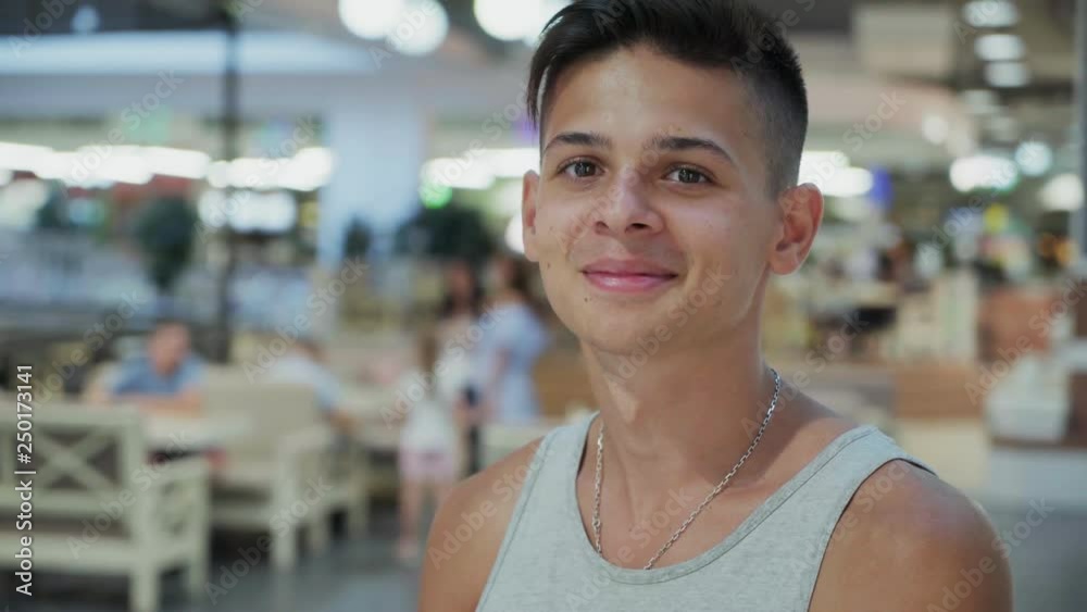 Happy teenager in A-shirt smiling and standing in a mall with people in summer Happy teenager in A-shirt smiling and standing in a mall with people in summer