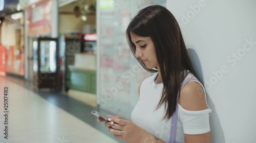 Gorgeous brunette girl browsing the net on her smartphone in a mall in summer  