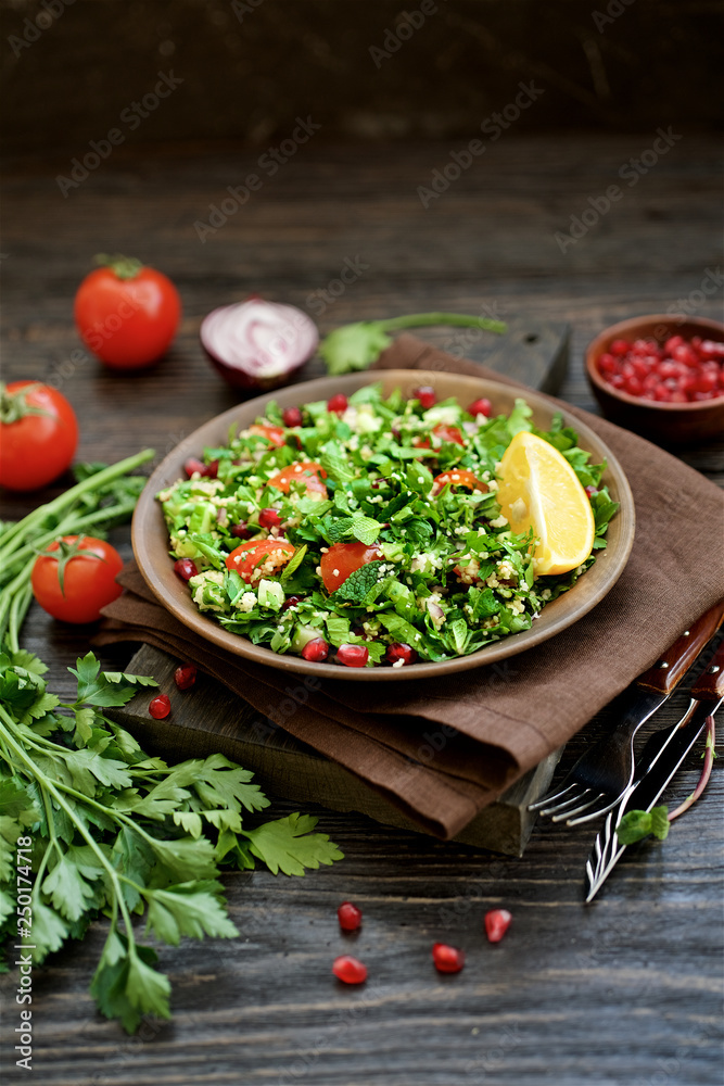 Traditional tabbouleh salad on dark brown wooden rustic background. Ingredients couscous, parsley, mint, onion, tomato. Close up view