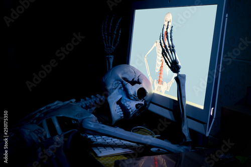 фотографія Fake human skeleton lying in front of desktop computer, computer addicted concept