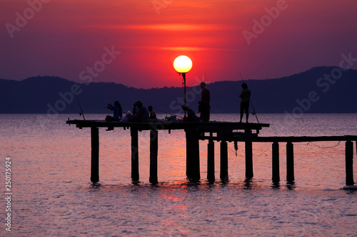 Silhouette of many people sit and stand enjoying fishingon the wooden bridge fishing the beautiful sunset  photo