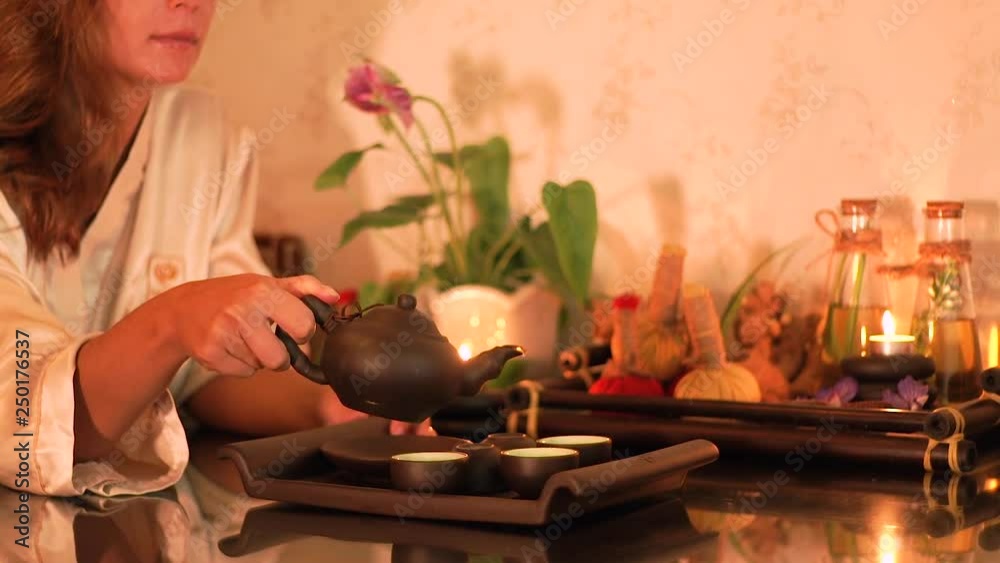 Young woman pouring hot chinese tea from teapot in cups for tasting. Woman pouring fresh green tea in cups for drinking after spa massage in beauty salon. Relaxation and recovery in oriental spa.