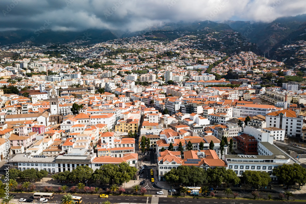 Urban landscape. Panorama of the city of Funchal. View of the city from the waterfront to the top of the mountains. In the mountains-fog over the city-the sun.