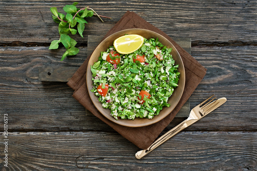 Traditional tabbouleh salad on dark brown wooden rustic background. Ingredients couscous, parsley, mint, onion, tomato. Close up view