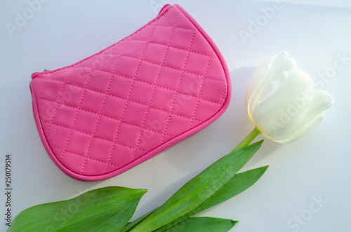 white tulip flower. pink cosmetic bag, makeup brushes, cosmetics on white background