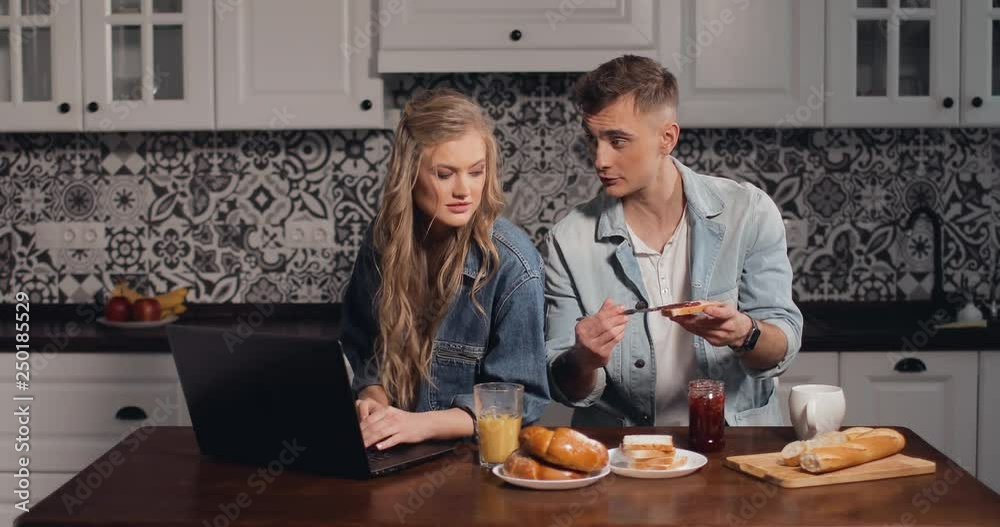 Girl using laptop in kitchen while couple having breakfast Girl using laptop in kitchen while couple having breakfast