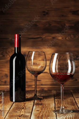 Glass and bottle with delicious red wine on table against wooden background