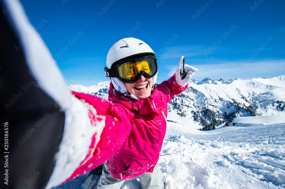 Selfie snowboarder. Young happy woman taking selfie with the smartphone on the top of the mountain