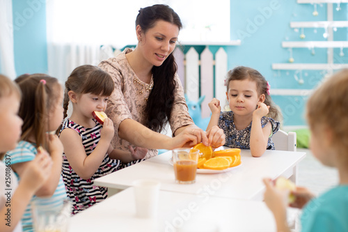 Children and carer together eating fruits in kindergarten or daycare