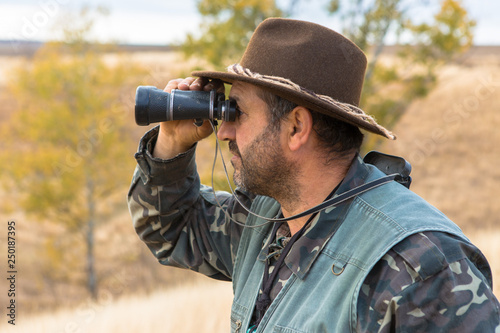 A hunter in a hat with binoculars looks out for prey 