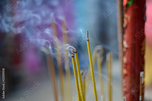 Small Asian incense sticks and a large red incense stick with Chinese characters are burning with blur and defocused background. Photo taken in ancient temple/ pagoda for over 250 years photo