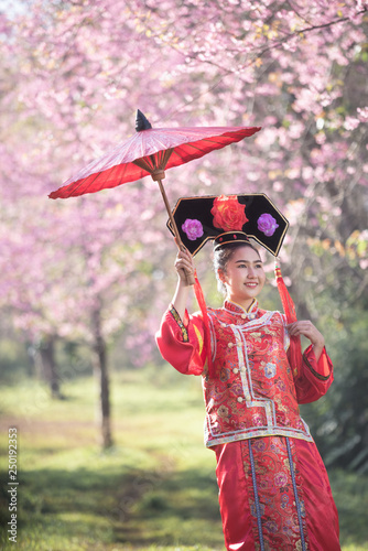 Beautiful Chinese young woman wearing red traditional cheongsam in cherry blossoms garden