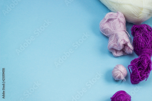 Products for needlework, knitting. Balls of pink, purple yarn on a blue background. Space for text.