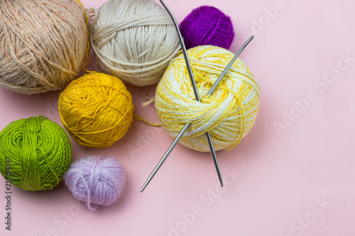 Products for needlework, knitting. Balls of yellow, green, purple yarn, knitting needles on a pink background. Space for text.