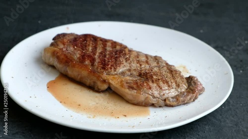 Fried beefstake on a white plate, somebody adding pepper, close up photo